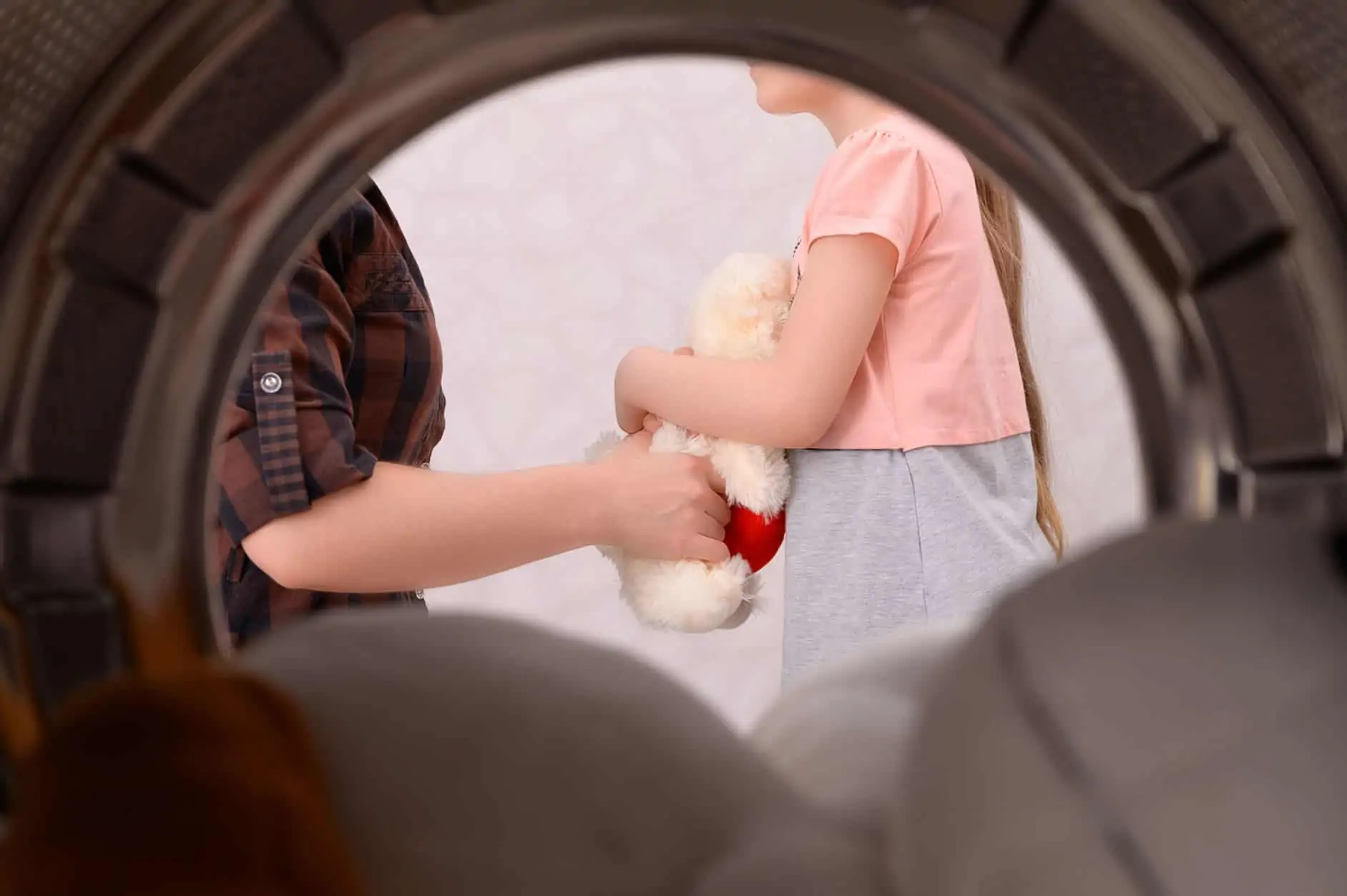 Babyspielzeug reinigen: Blick aus der Waschmaschine heraus auf Mutter und Kind mit Kuscheltier