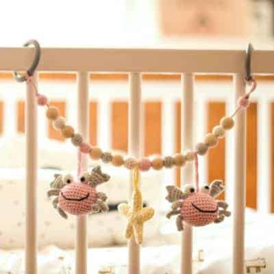 Gehäkelte Kinderwagenkette Krabbe PINCER in Rosa mit Befestigungsringen am Kinderbett